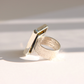 A silver amber ring with a textured band and a geometric, angular flat top, photographed on a white surface with soft shadows.
