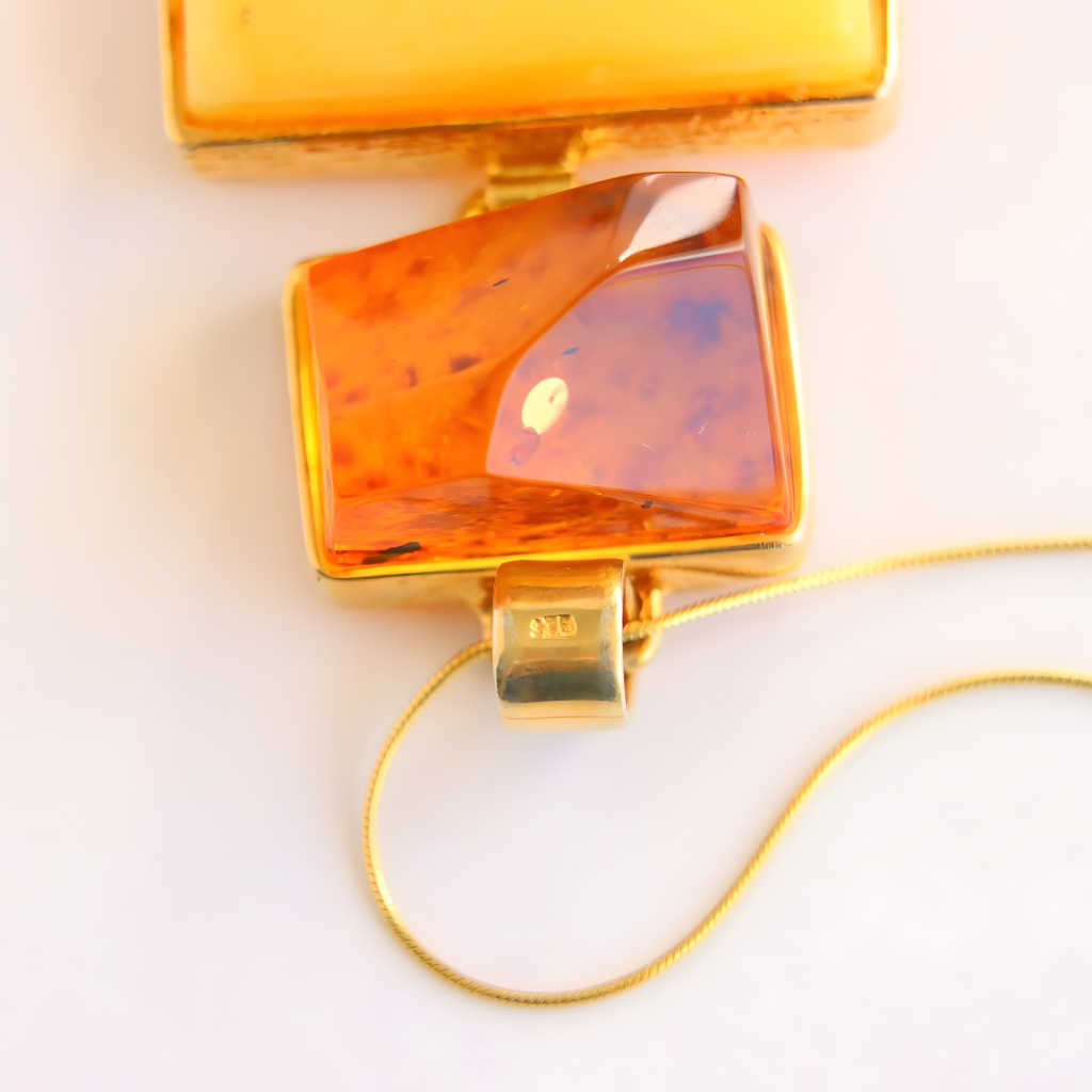 Gold statement necklace with a large amber-colored pendant on a light background