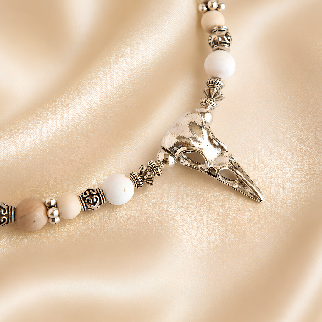 raven skull Necklace pendant and white beads on a beige background
