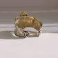 A wide silver amber cuff bracelet with engraved Greek key patterns and a central medallion, photographed on a white surface with soft shadows.
