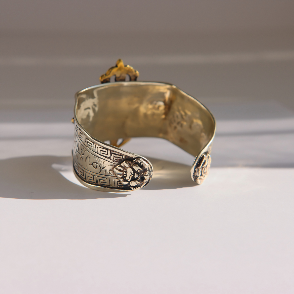 A wide silver amber cuff bracelet with engraved Greek key patterns and a central medallion, photographed on a white surface with soft shadows.