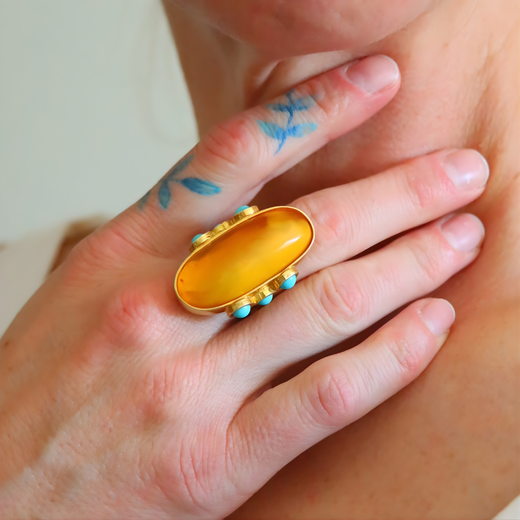 Hand wearing a gold amber ring with a large amber stone and turquoise accents.