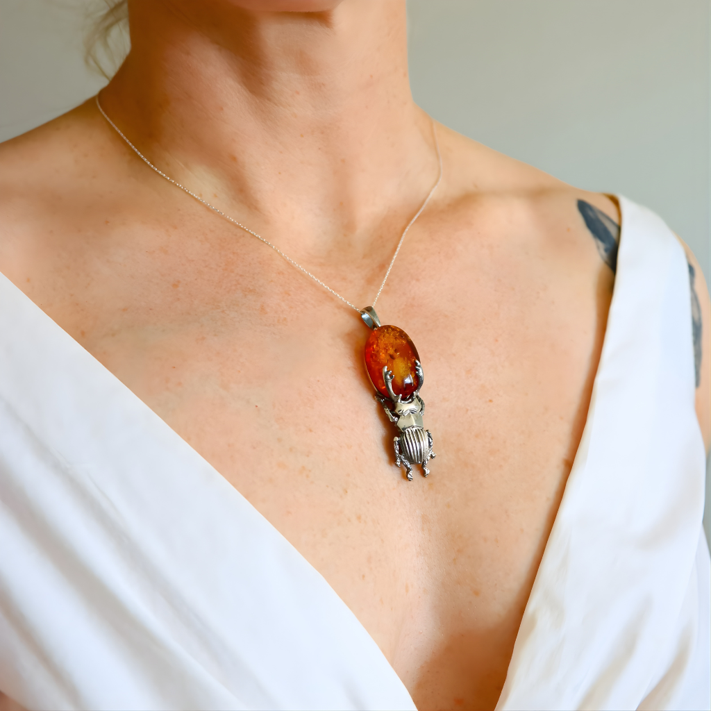 Necklace with a amber pendant featuring an amber-colored stone and silver insect design on a person wearing a white top.