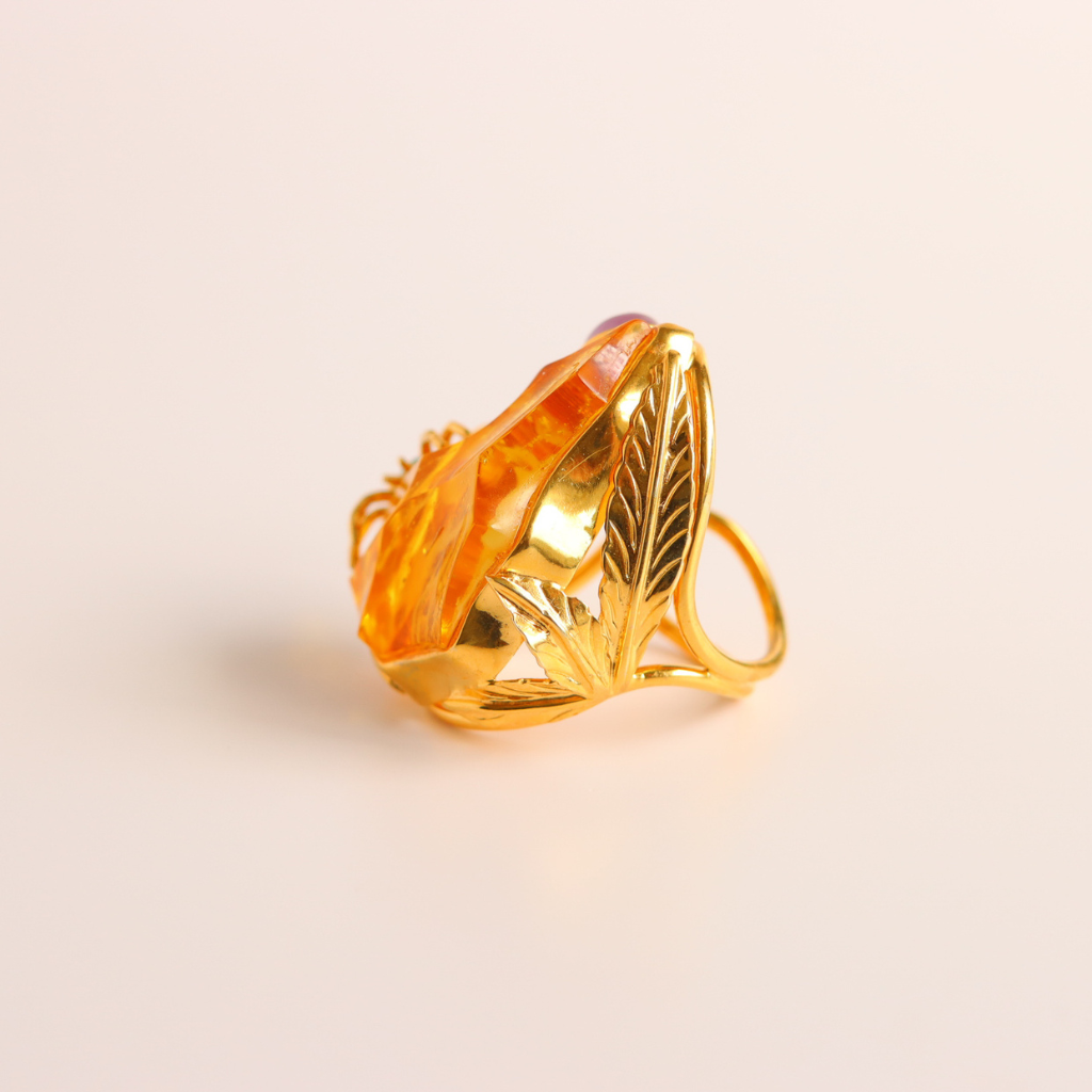 Gold cocktail ring with a large orange gemstone on a beige background