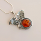 Silver dragon-shaped pendant with amber stone on a beige background