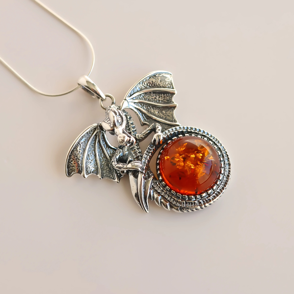 Silver dragon-shaped pendant with amber stone on a beige background