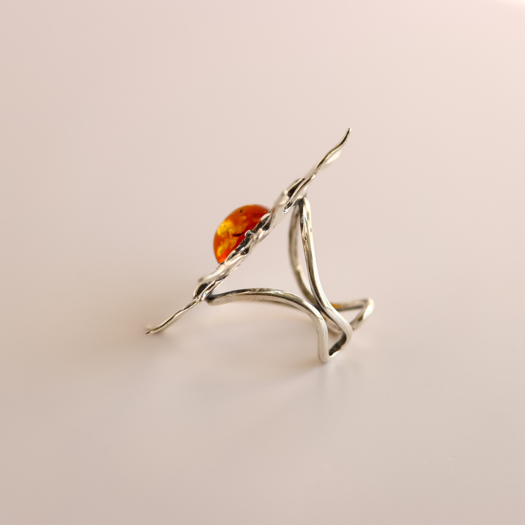 Silver sun ring with a orange stone on a light pink background