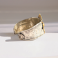 A wide silver amber cuff bracelet with engraved Greek key and scroll motifs, accented by small gold-toned decorative elements on a white background.