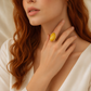 Woman wearing a gold amber ring with a yellow gemstone on a neutral background