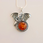 Silver Dragon-shaped pendant with amber-colored stone on a beige background