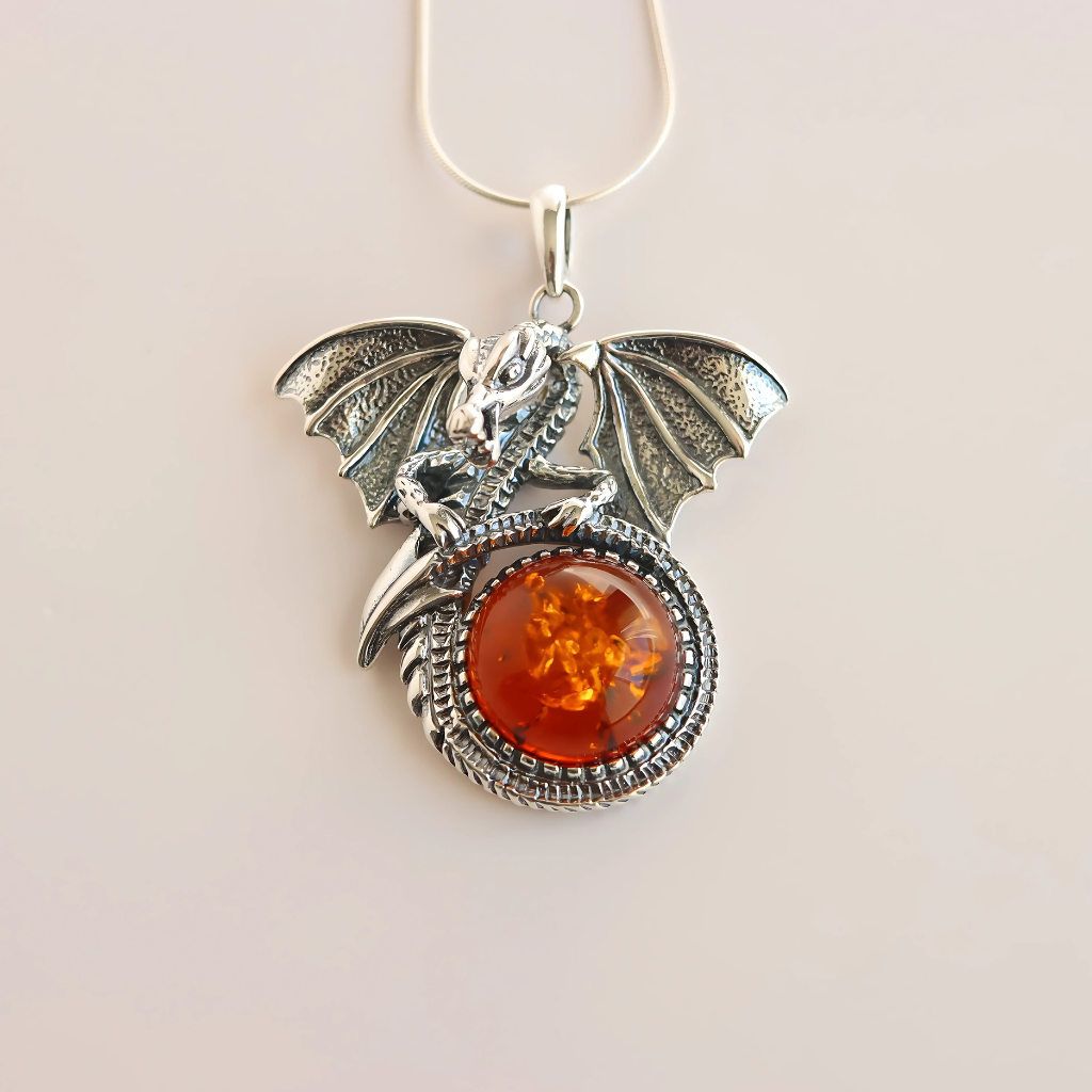 Silver Dragon-shaped pendant with amber-colored stone on a beige background