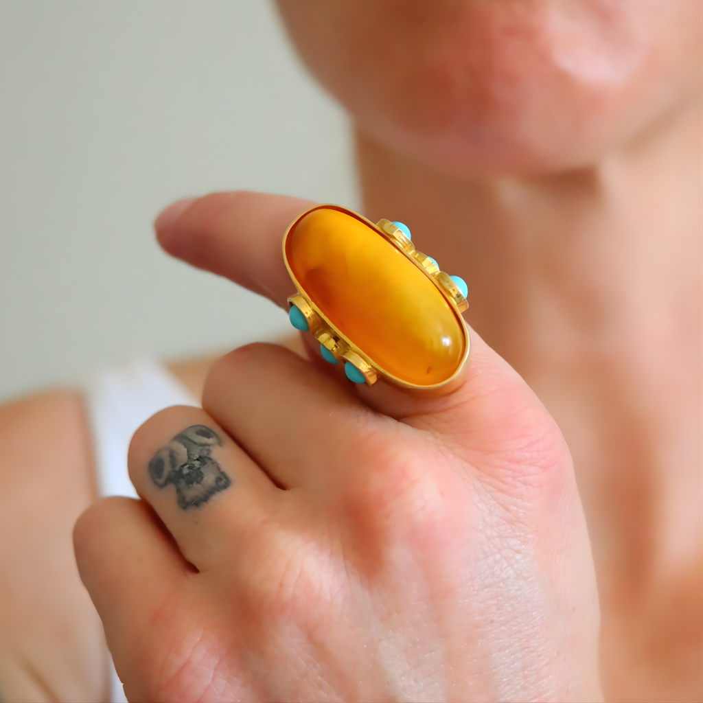 Close-up of a hand wearing a gold amber ring with a large amber stone and turquoise accents.