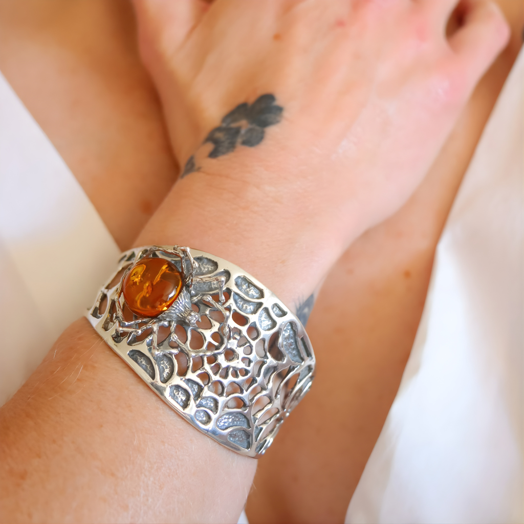 Silver spider amber bracelet with amber stone on a wrist against a white background