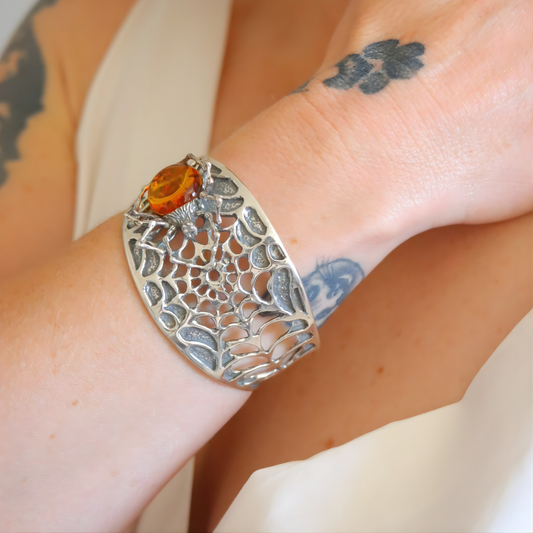 silver spider amber bracelet with a central cognac amber stone on a wrist with tattoos