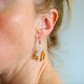 Close-up of a person wearing a spider web amber earring with orange gemstones.