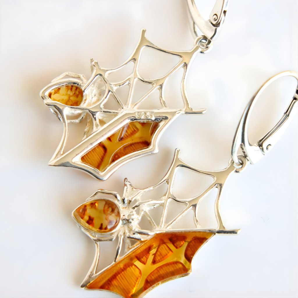 Silver amber earrings with spiderweb design and amber-colored stones on a white background