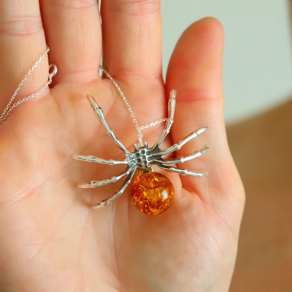 amber necklace Spider-shaped pendant with an orange sphere held in a hand