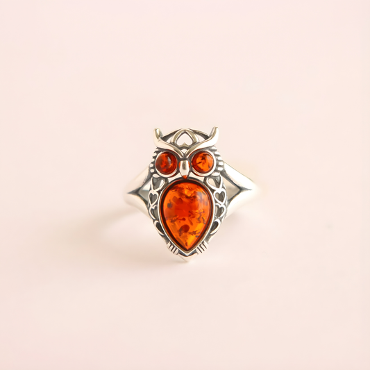 Silver owl amber ring with amber-colored stones on a beige background