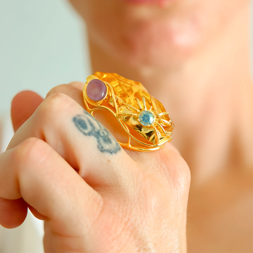 Gold cocktail ring with gemstones on a person's finger against a blurred background