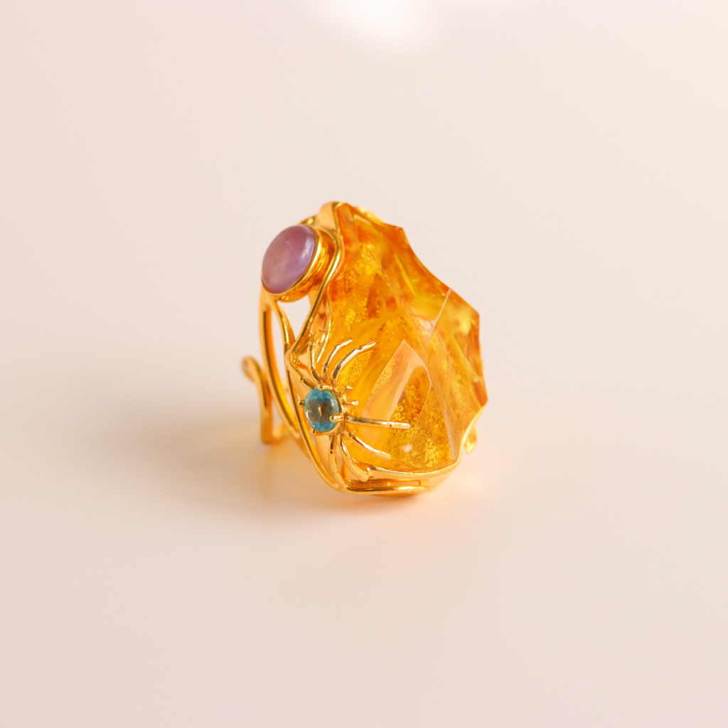 Gold cocktail ring with amber and gemstones on a beige background