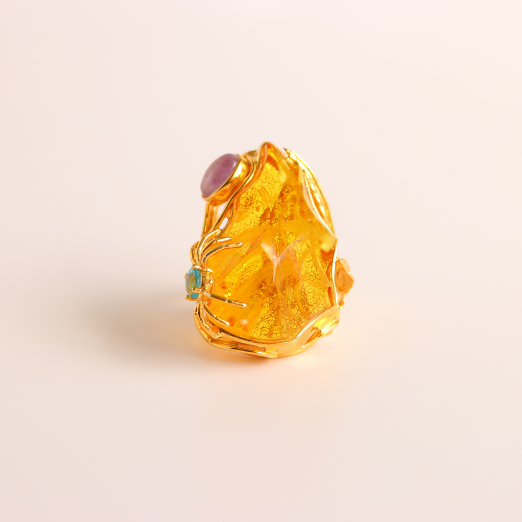 Gold cocktail ring with a central gemstone on a light beige background