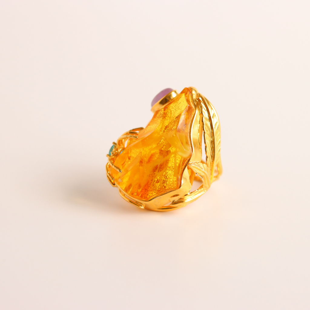 Gold cocktail ring with a large amber stone on a light beige background