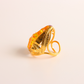 Gold cocktail ring with a large orange gemstone on a light beige background