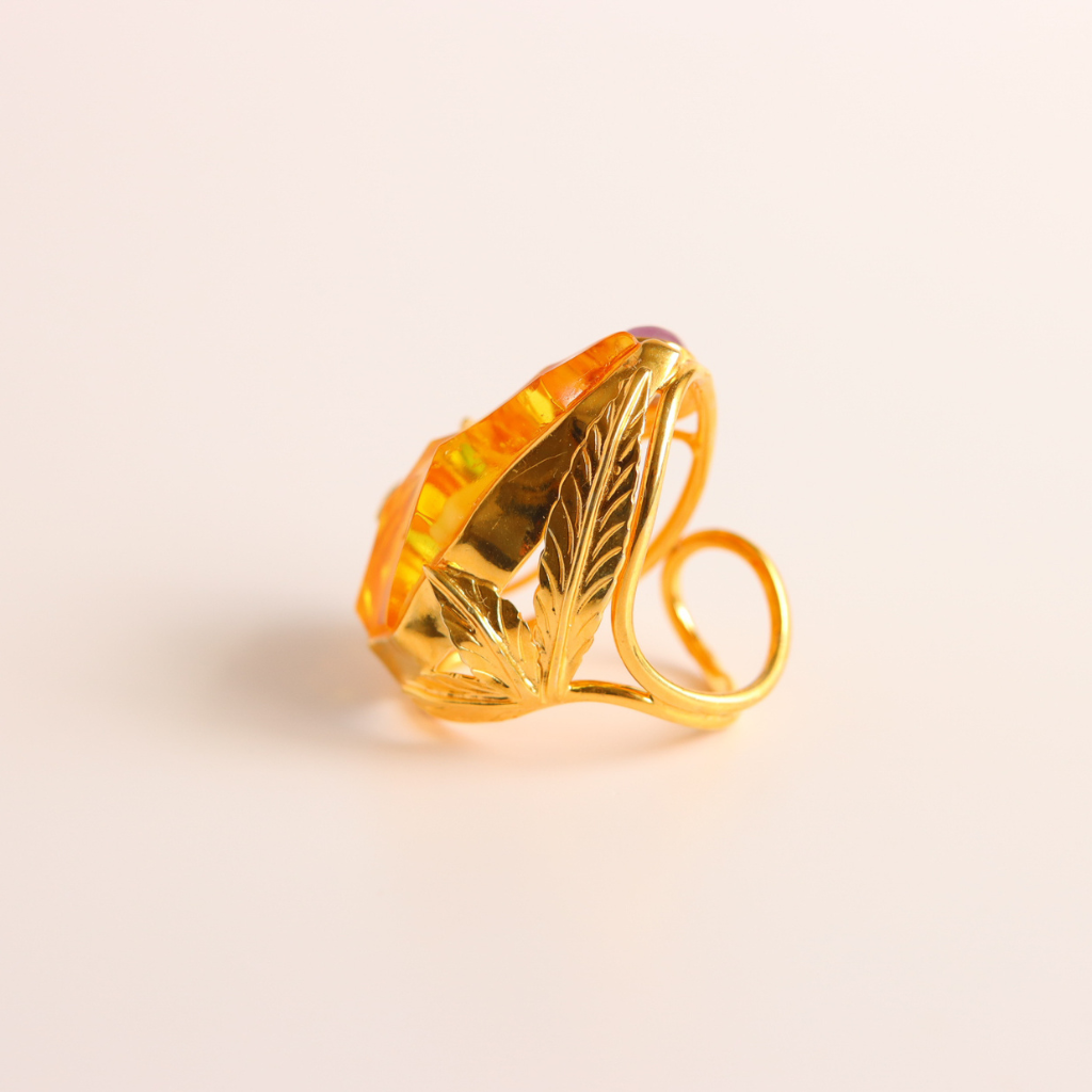 Gold cocktail ring with a large orange gemstone on a light beige background