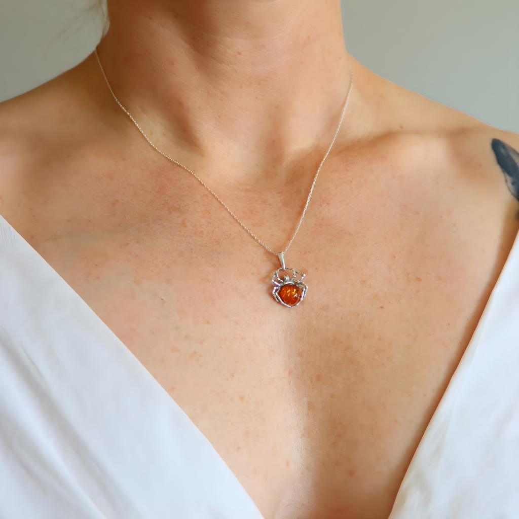 Necklace with a silver amber spider pendant worn by a person in a white top.