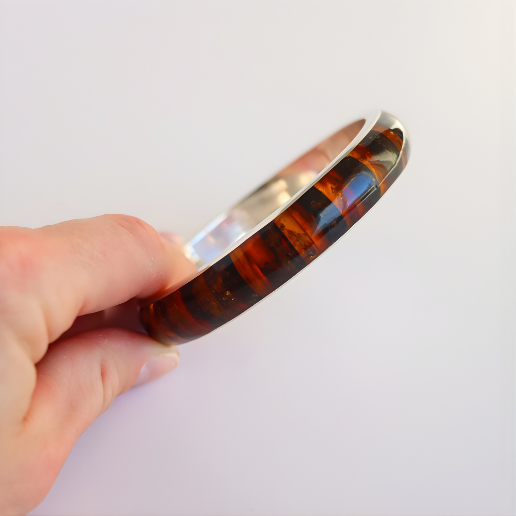 Hand holding a amber bangle bracelet against a white background