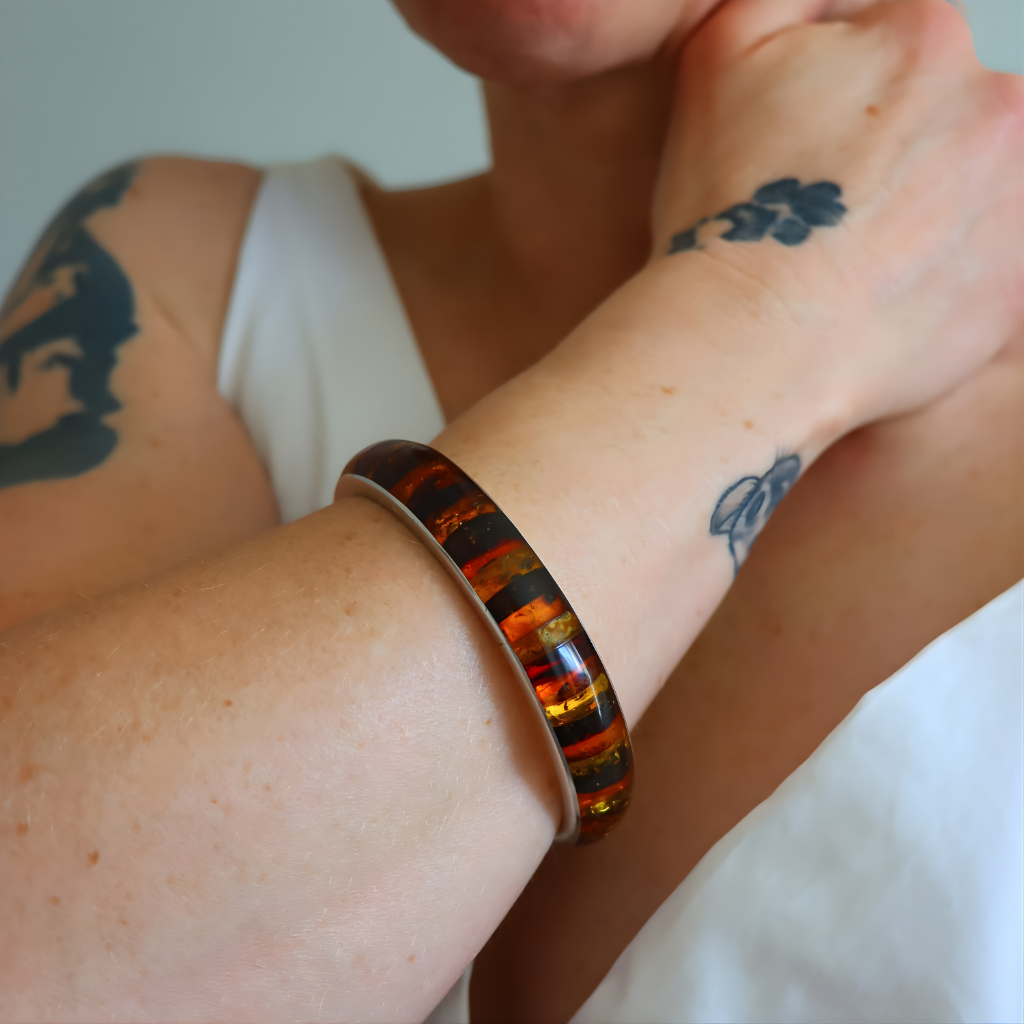 Close-up of a person's arm wearing a colorful bangle bracelet with tattoos visible on the skin.