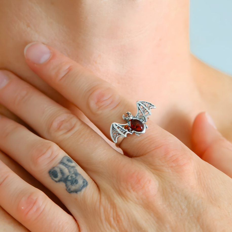 Silver bat ring with a red gemstone on a person's finger