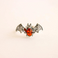 Bat ring with amber-colored gem on a beige background