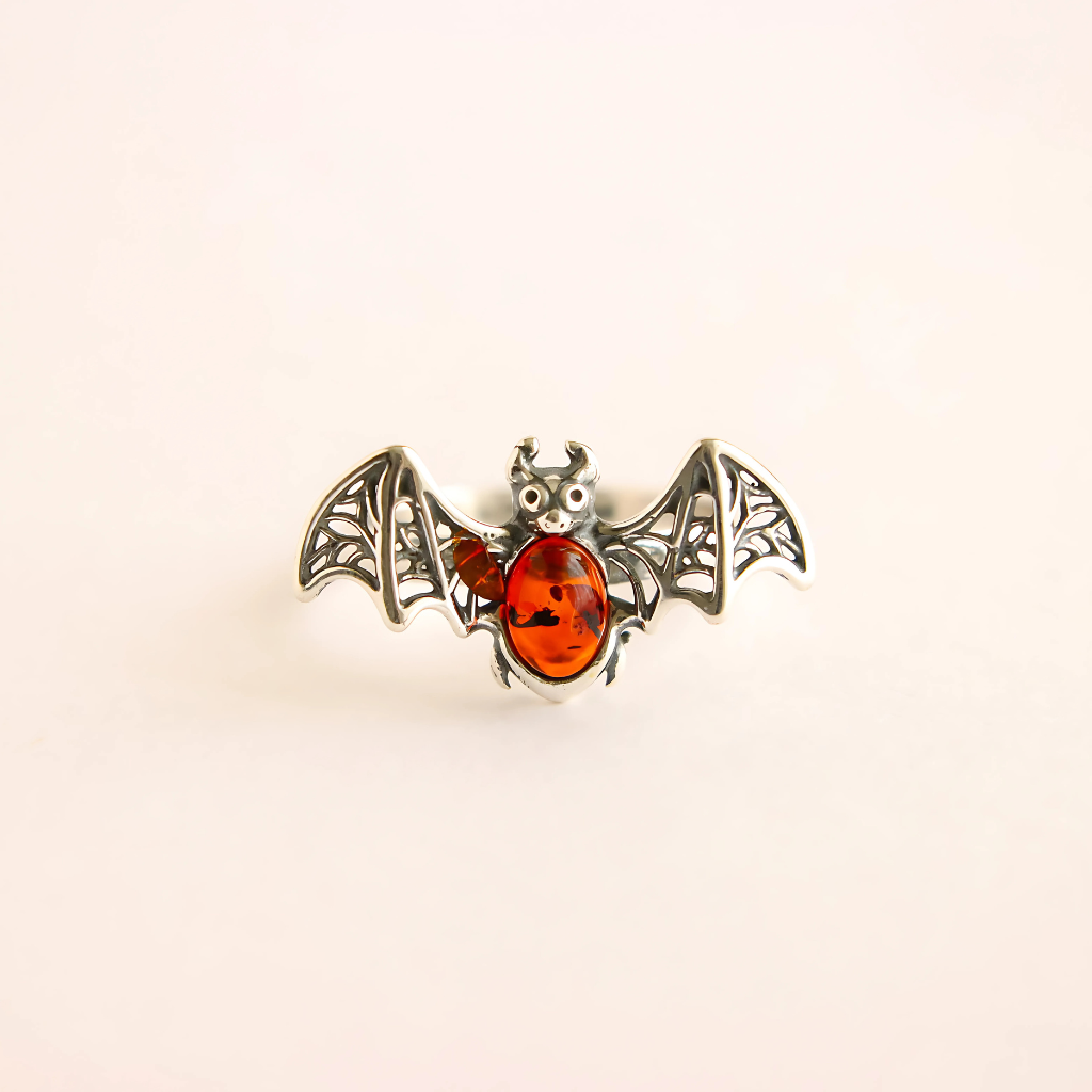 Bat ring with amber-colored gem on a beige background