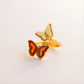 gold Butterfly ring with red and white wings on a light gray background