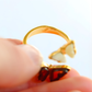 Gold butterfly ring with heart-shaped gemstones held between fingers against a white background