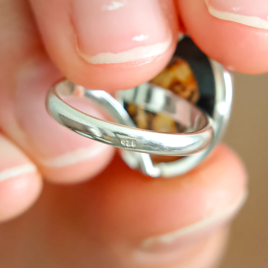 Close-up of a silver mushroom ring held between fingers with a blurred background