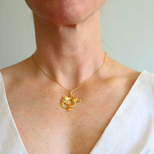 Gold necklace with a dragon pendant worn by a person against a neutral background