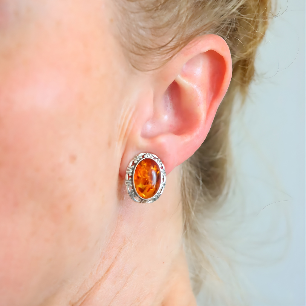 Close-up of an ear wearing a silver clip on earring with amber stone.