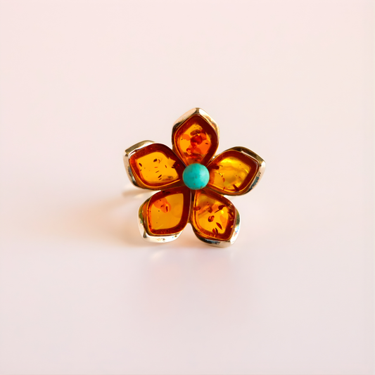 Flower ring with amber and turquoise center on a light pink background