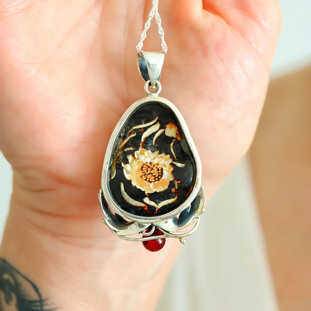 amber necklace with floral design held in a hand