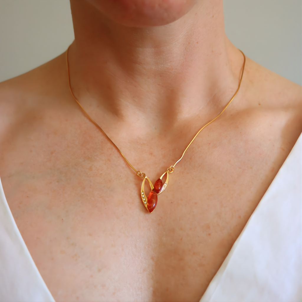 Gold amber necklace with a red pendant on a person wearing a white top.