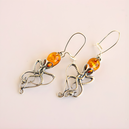 Pair of  Baltic amber octopus dangle earrings  with amber beads on a light pink background