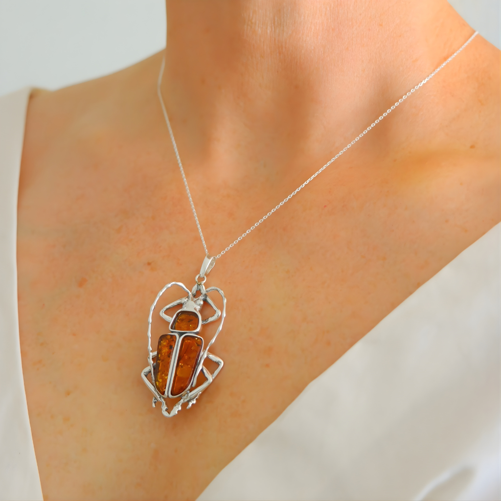 Necklace with a scarab pendant featuring amber stones on a person wearing a white top.