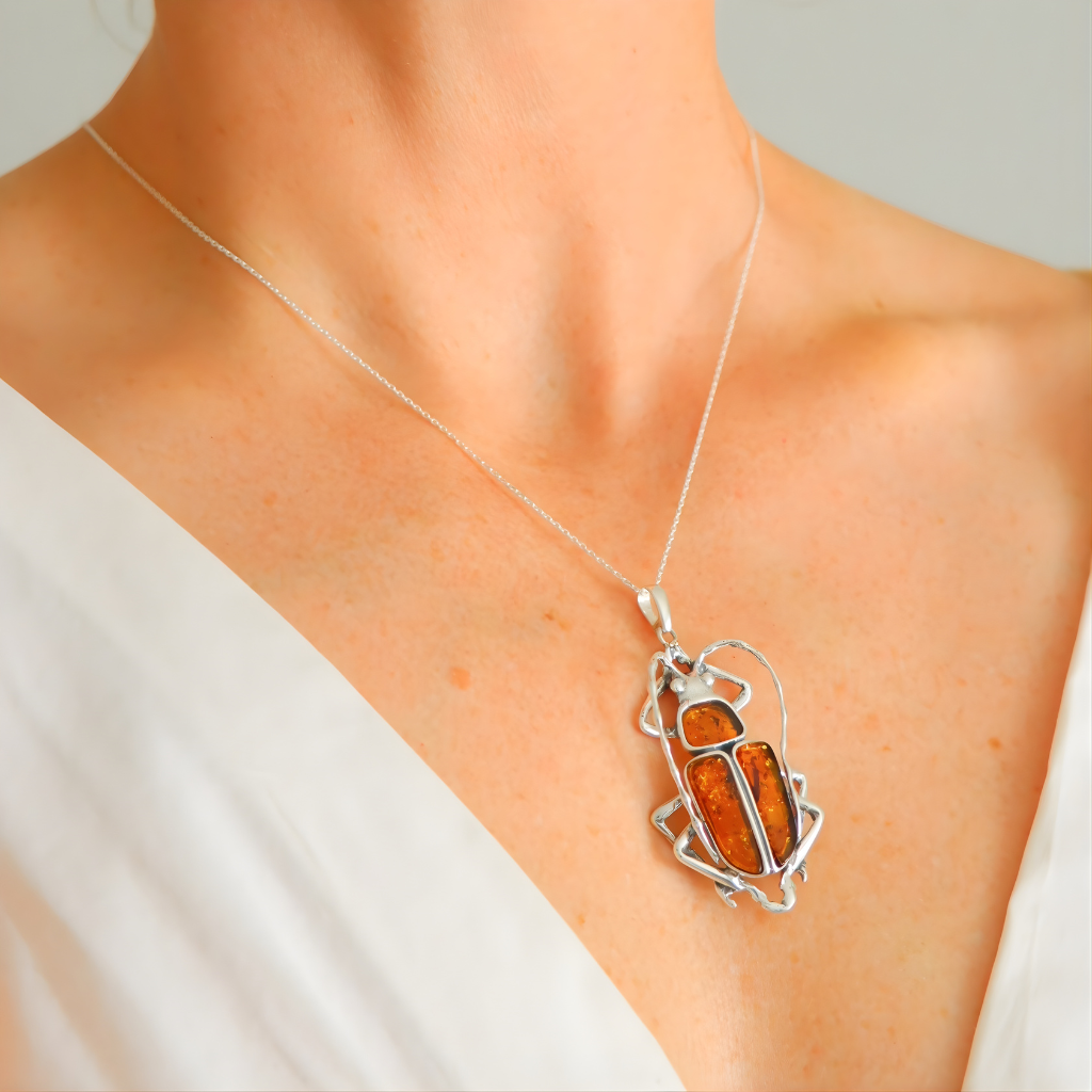 Necklace with a scarab pendant featuring orange stone and silver frame on a person wearing a white top.