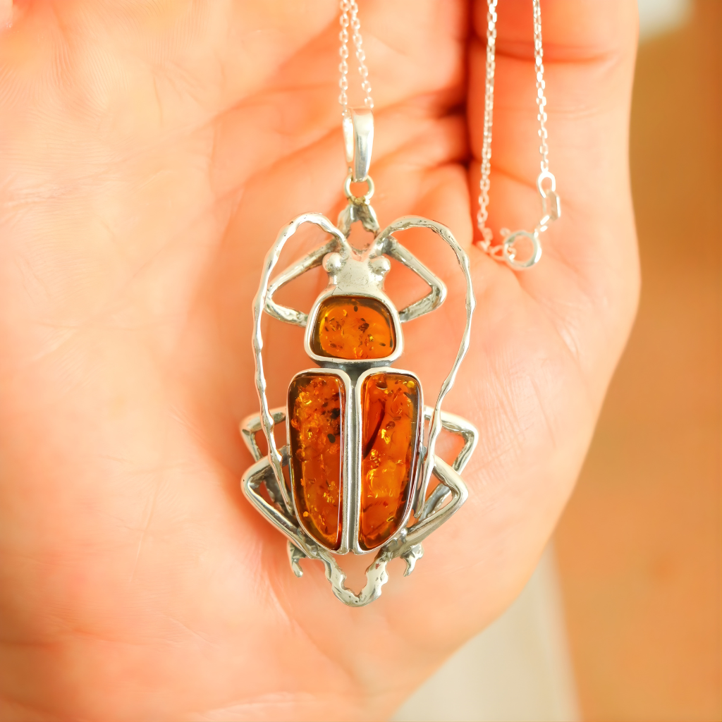 Silver scarab pendant with amber-colored stone held in a hand against an orange background