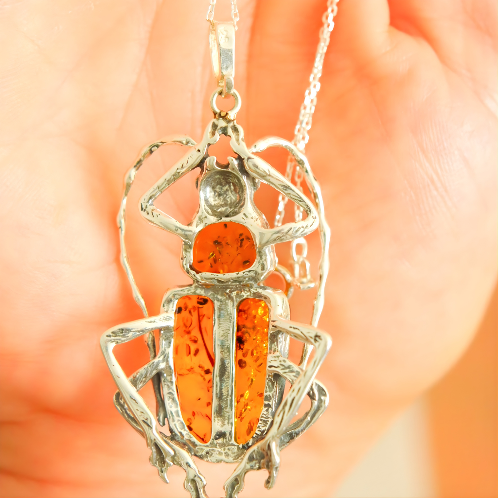 Silver scarab pendant with orange central stone held by a hand against a blurred background