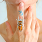 Close-up of a hand wearing a silver scarab ring with amber stones on a light background