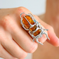 Silver scarab ring with amber stones on a hand against a blurred background