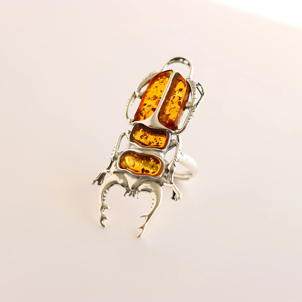 Silver scarab ring with amber stones on a light beige background